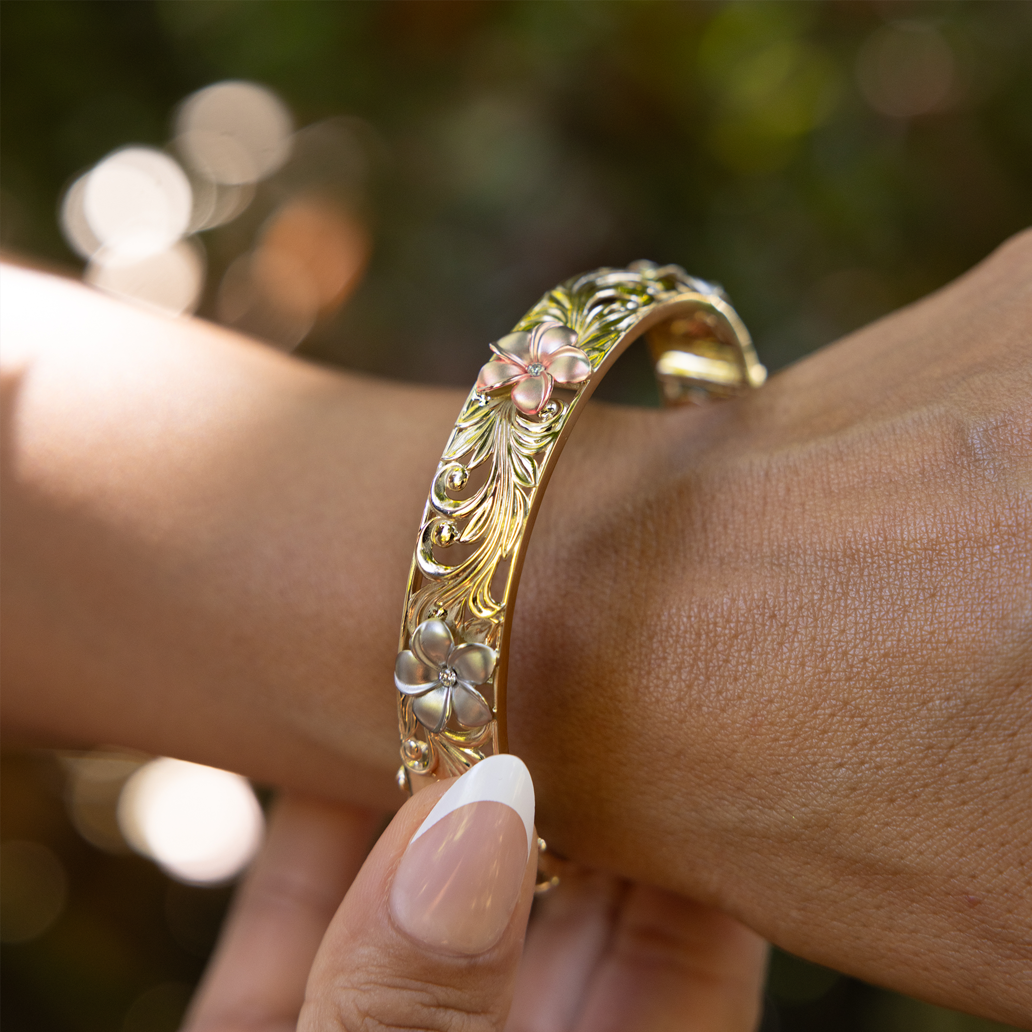Close up of Hawaiian Heirloom Plumeria Hinge Bracelet in Tri Color Gold with Diamonds - 12mm on womanʻs wrist